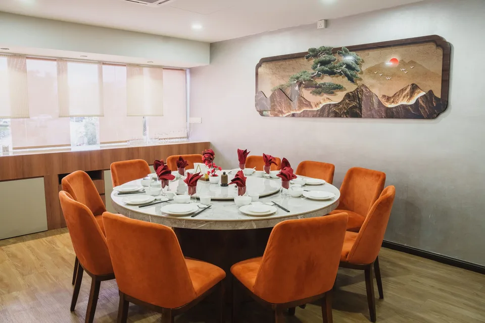 A round dining table set with white plates and red napkins, surrounded by terracotta chairs at Chī Hǎo TTDI.