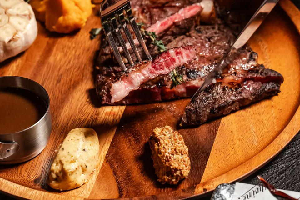 Sliced grilled beef served on a wooden board with roasted garlic, sauces and accompaniments at The Brick by Justwine.